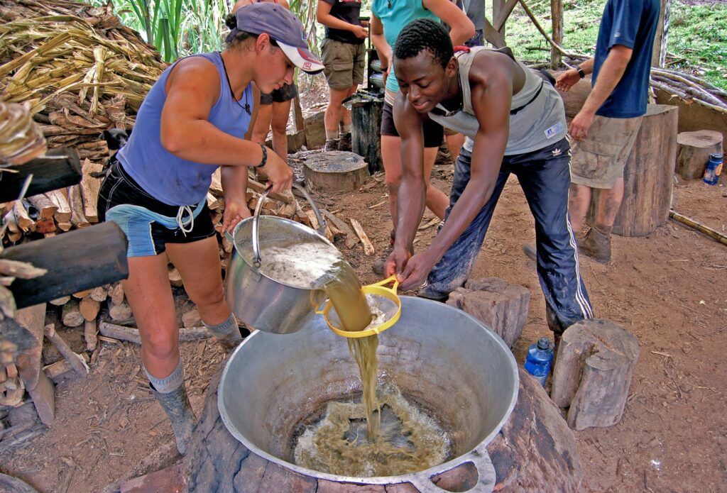 People pouring liquid into a large pot.