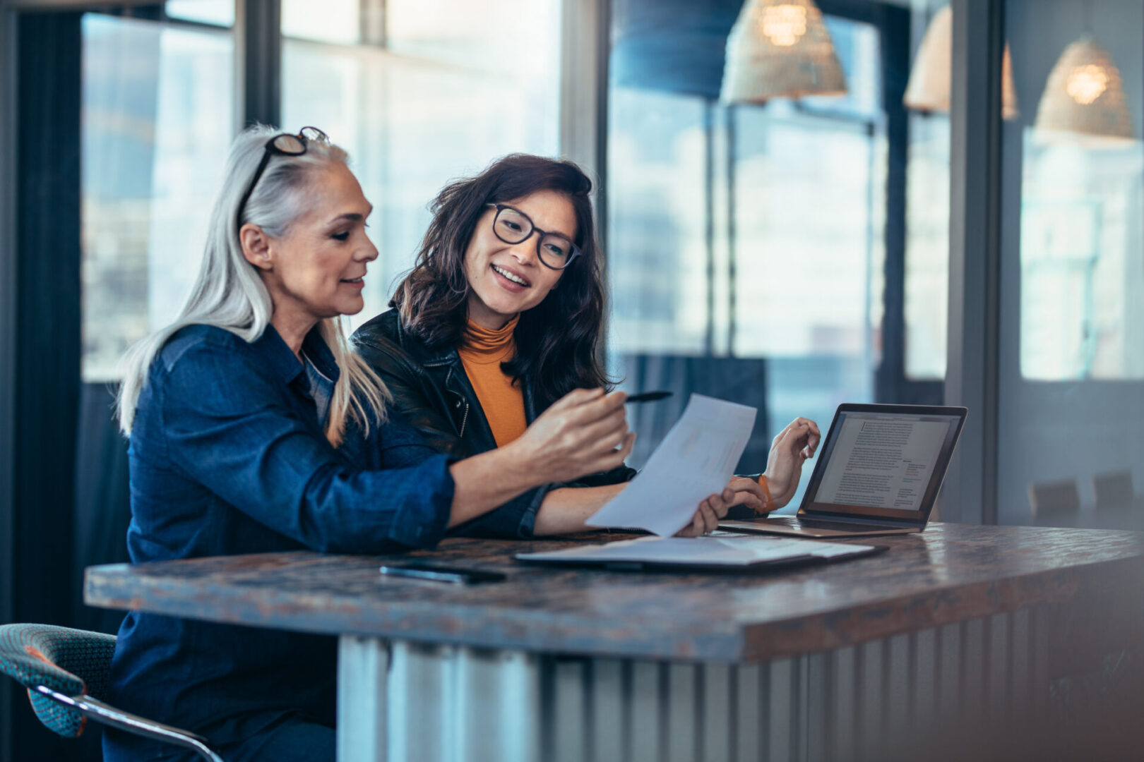 Two women analyzing documents while sitting on a table in office. Woman executives at work in office discussing some paperwork.